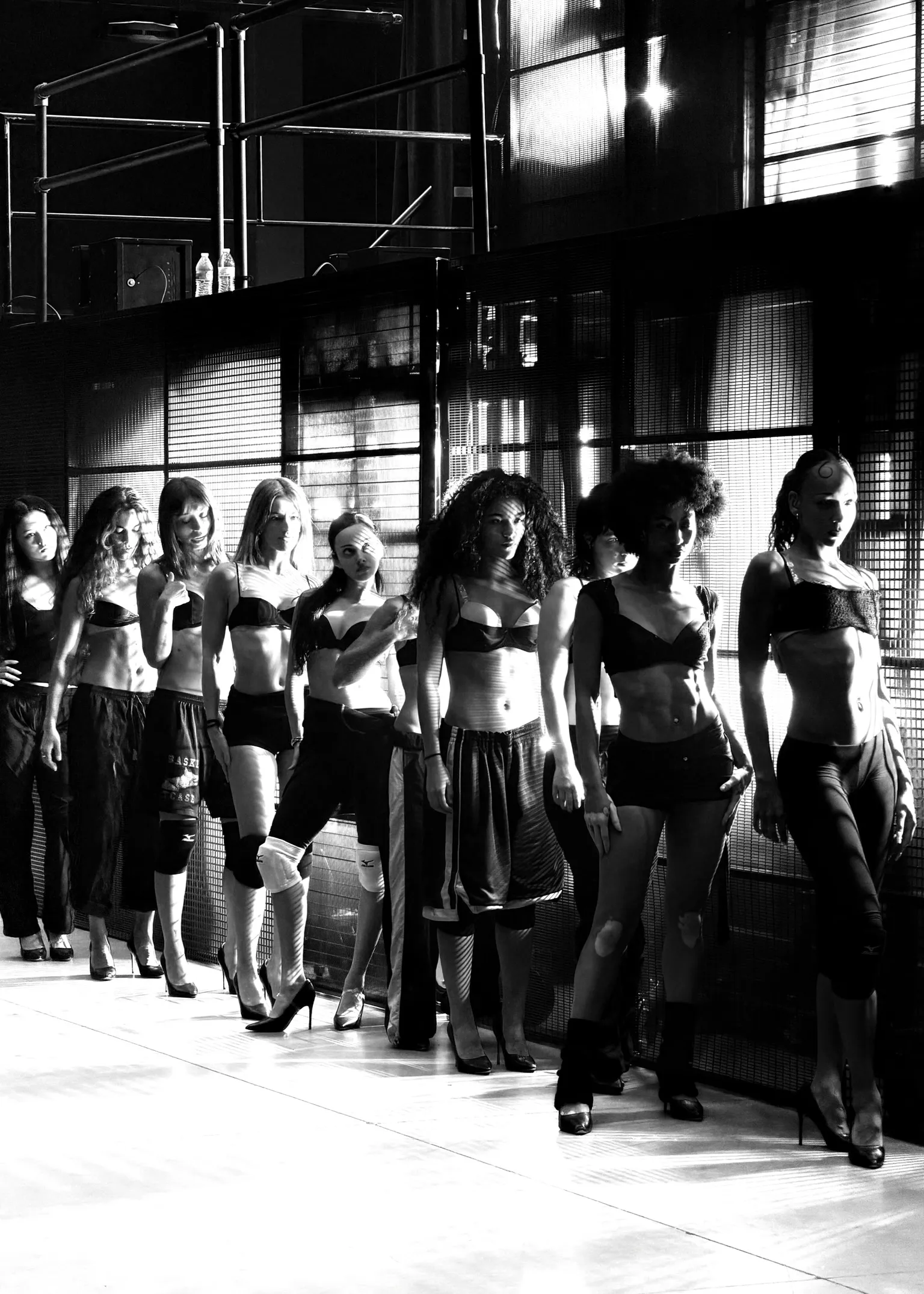 Black-and-white image of dancers lined up backstage in performance outfits and heels.