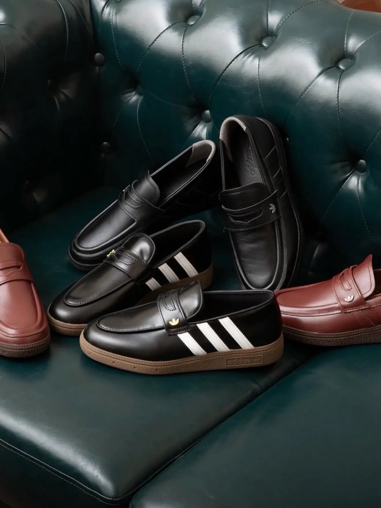 Four pairs of loafers arranged on a dark green tufted leather chair, including black shoes with white stripes and burgundy