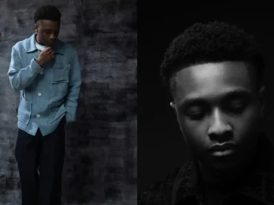 Miles Caton Wear A Light Blue Textured Jacket And Black Trousers Against A Dark Mottled Studio Backdrop