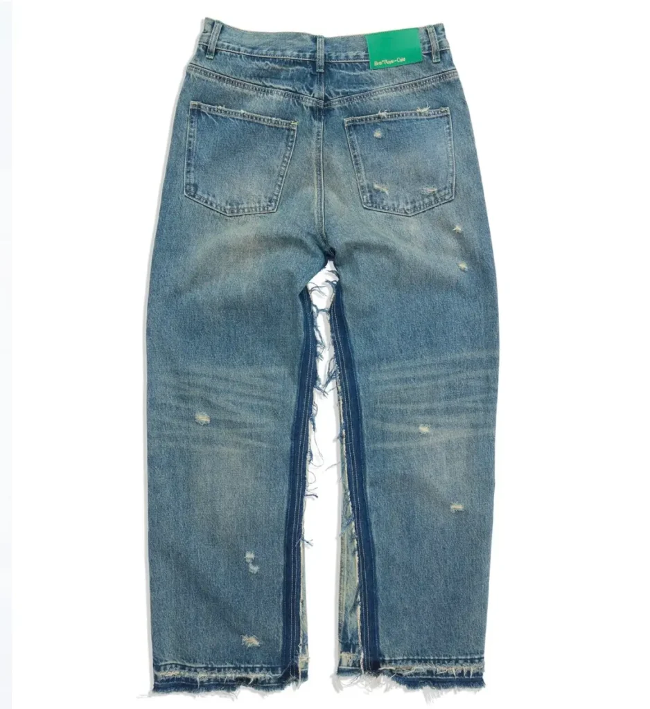 Back view of the distressed wide-leg jeans featuring large rear pockets, faded wash, frayed hems, exposed inner-leg construction, and a green Birth®RoyalChild waistband patch