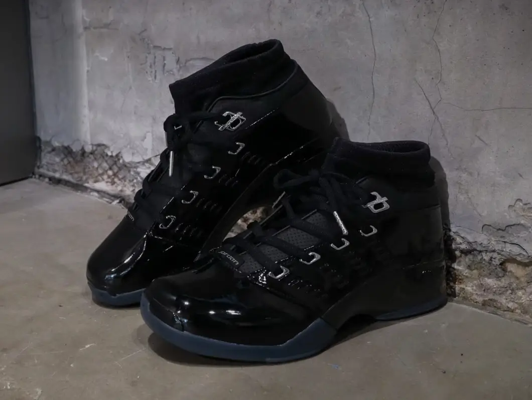 Pair of glossy black Jordan high-tops positioned against a distressed concrete wall.