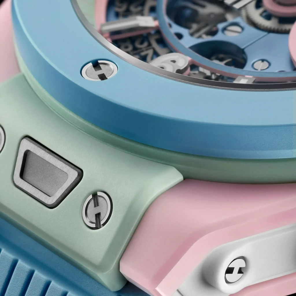 Hublot Big Bang watch close-up highlight the pastel blue bezel, mint green case section, pink ceramic body, exposed dial component, and polished H-shape screw