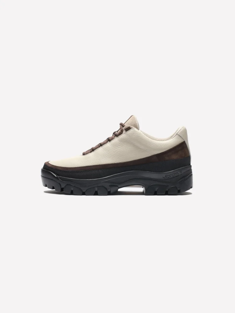 Off-white leather hiking shoe with brown suede mudguard, brown laces, and a black Vibram platform sole