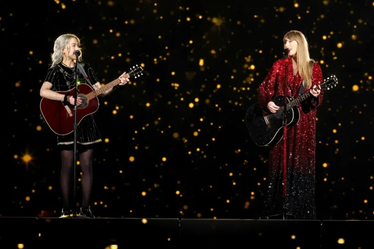 Phoebe Bridgers perform guitar opposite Taylor Swift in a sparkle red-and-black gown on a stage fill with golden light