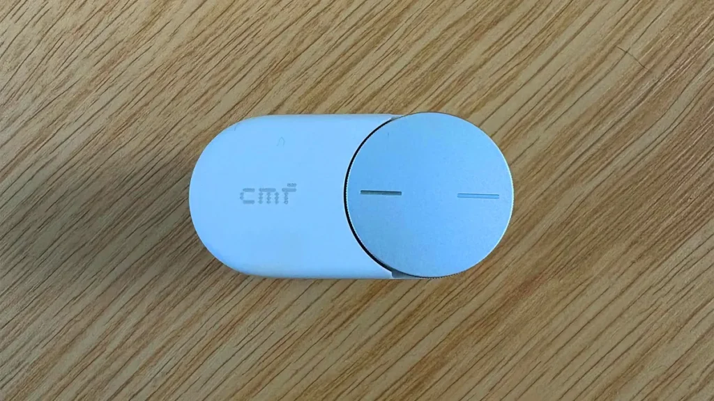 Close-Up Top View Of The CMF Clip Pro Charge Case And Circular Silver Smart Dial On A Wooden Surface