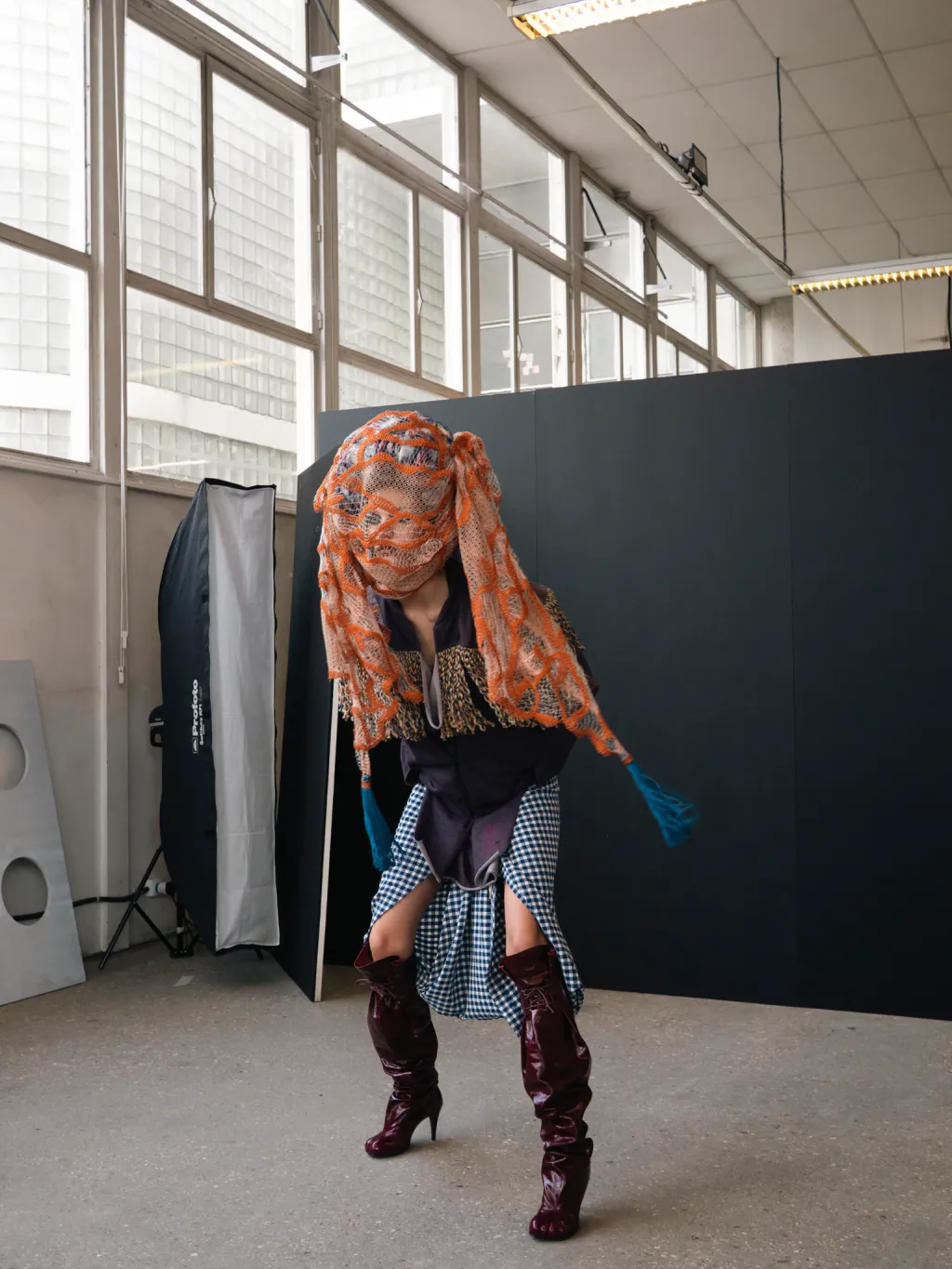 Andreas Kronthaler For Vivienne Westwood Autumn-Winter 2026/27 Backstage Look Featuring An Orange Netted Headpiece, Layered Gingham Skirt And Burgundy Boots