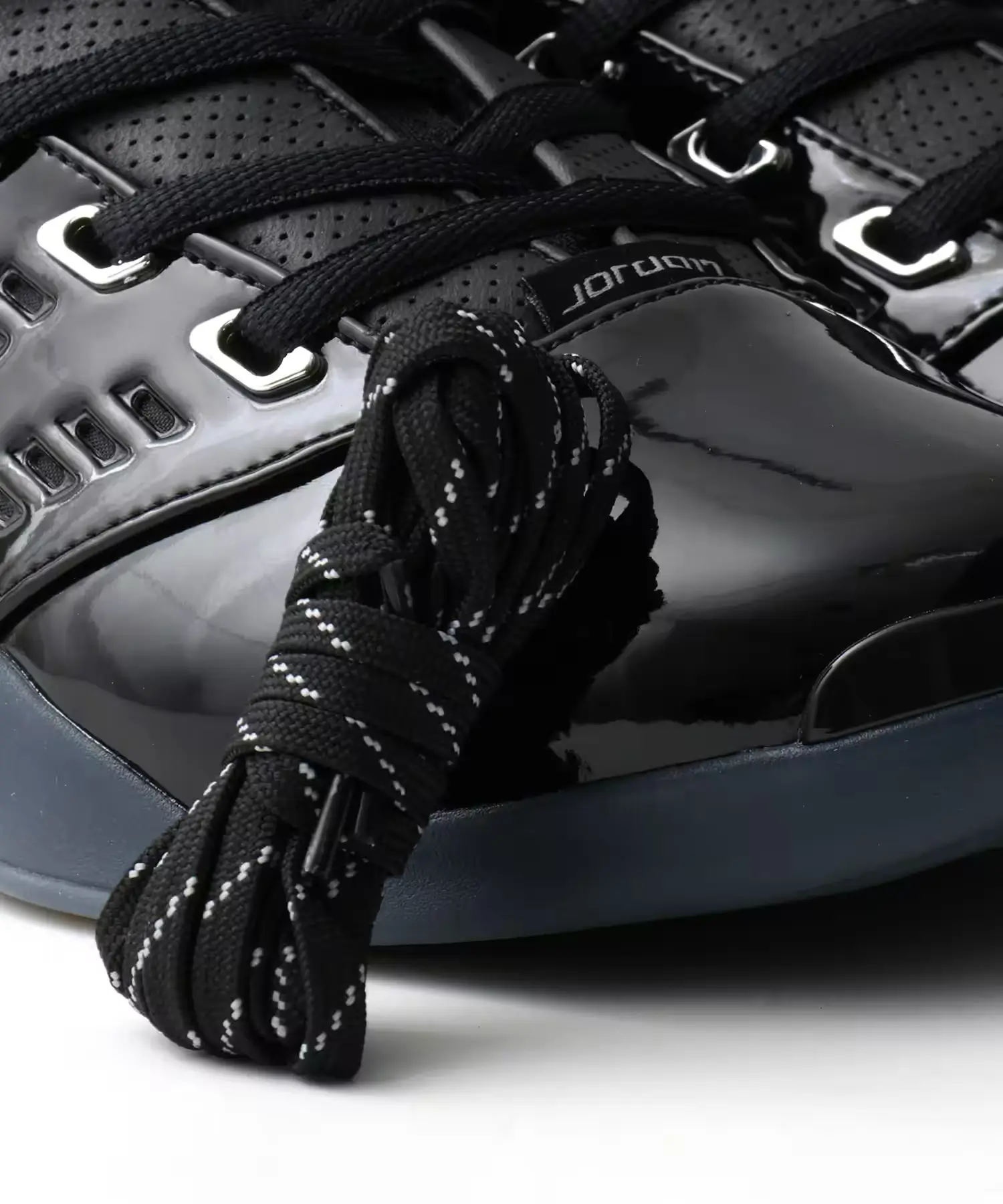 Close-up of glossy black Jordan shoes with silver eyelets and black-and-white speckled spare laces.