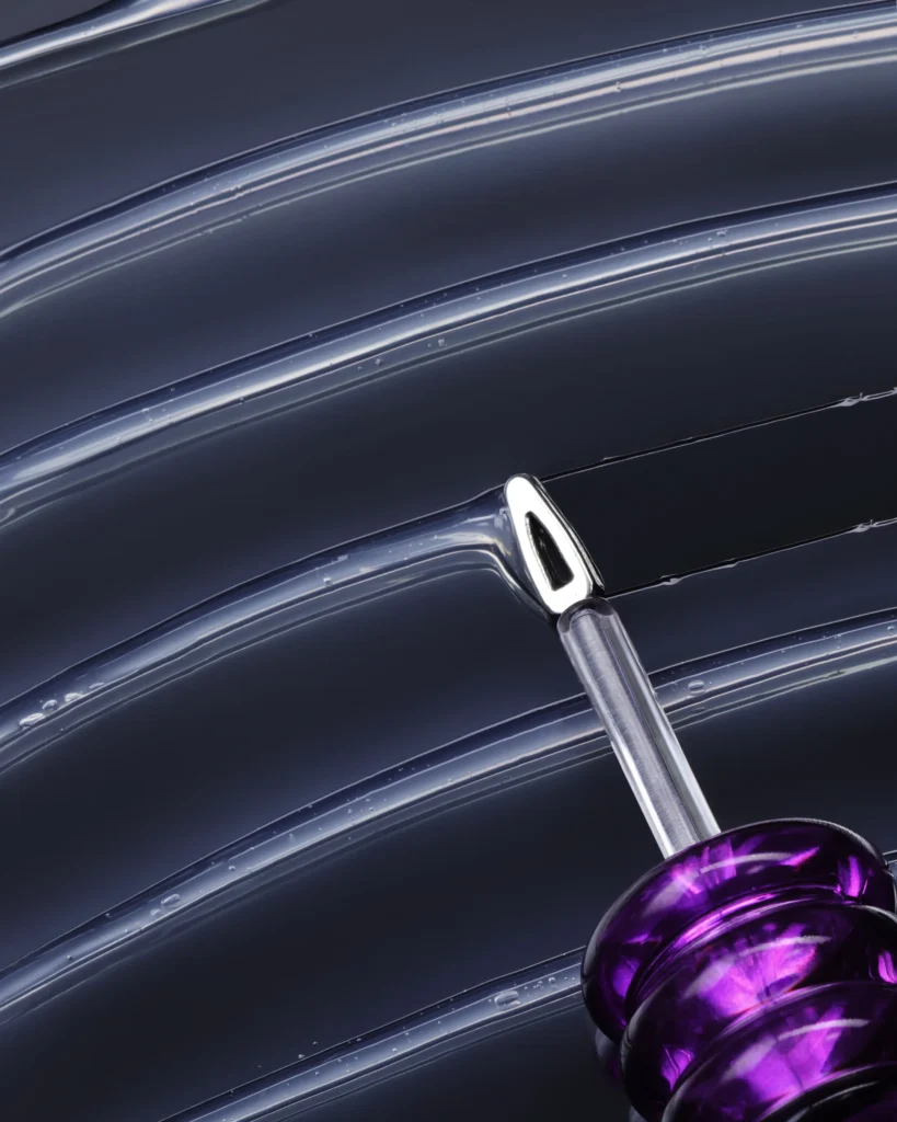 Close-up of Laka’s clear gloss applicator sweep through transparent gel, framedby a sculpture purple handle against a dark background