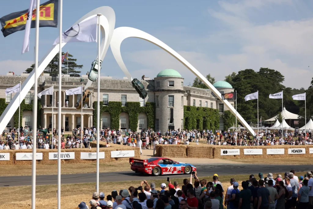 Race Car Number 76 Drive Past Crowd And Goodwood’s Central Automotive Sculpture