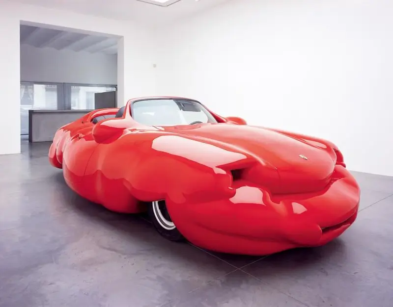 Erwin Wurm's 'Fat Convertible' sculpture, a glossy oversized red car with exaggerated rounded proportions displayed inside a minimalist white gallery.