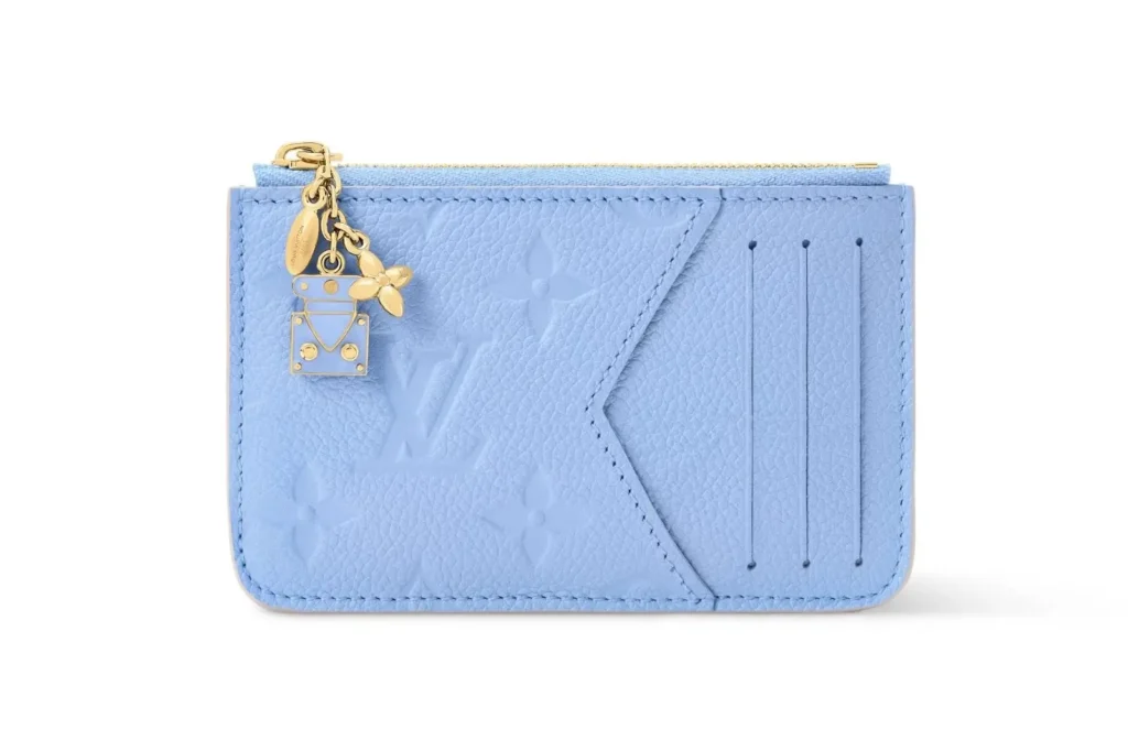 Light blue Monogram Empreinte leather card holder with embossed logo pattern, angled card slot, zip compartment, and gold-tone charm