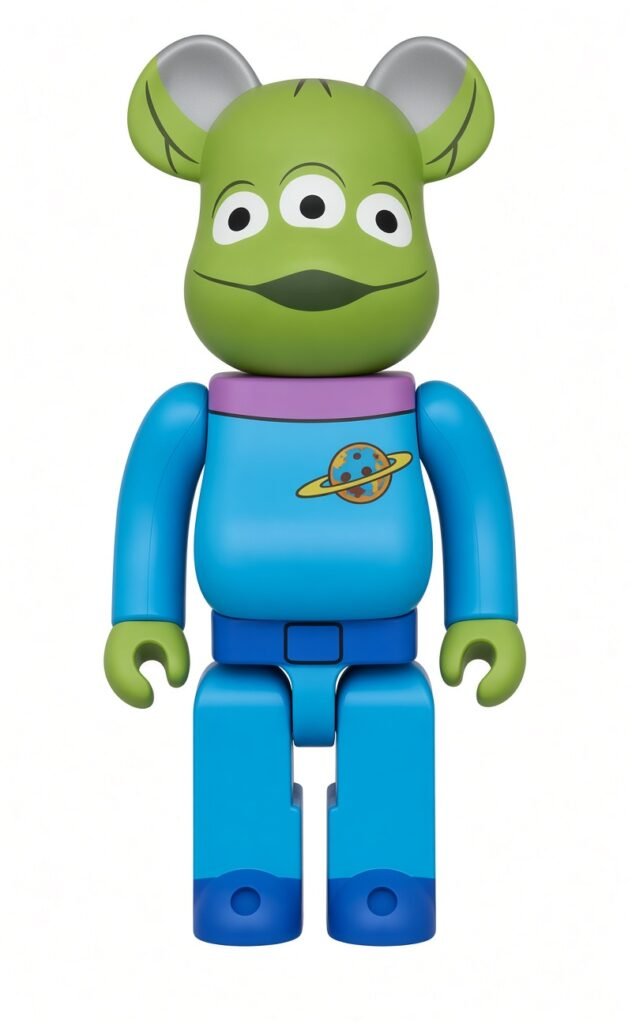 Green alien BE@RBRICK figure with three eyes, gray ears, blue body, and a planet emblem on its chest