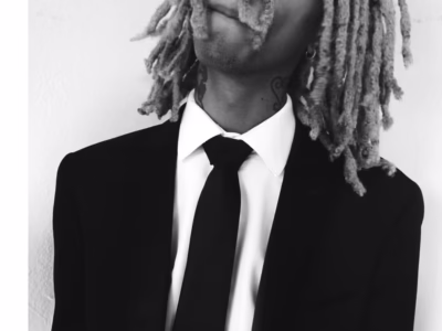 Monochrome Portrait Of prettifun With Long Dreadlocks Wearing A Black Suit, White Shirt, And Tie While Looking Upward