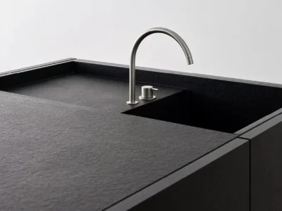 Close-up of a min black kitchen island with an integrated dark sink and curved brushed-metal faucet against a clean white wall