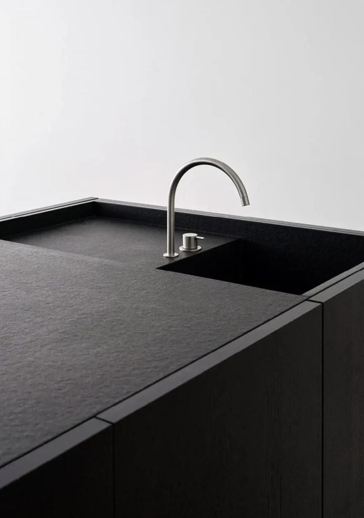 Close-up of a min black kitchen island with an integrated dark sink and curved brushed-metal faucet against a clean white wall