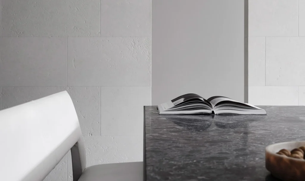 Min dine area with a dark stone table, white chair, open book, and texture white stone wall