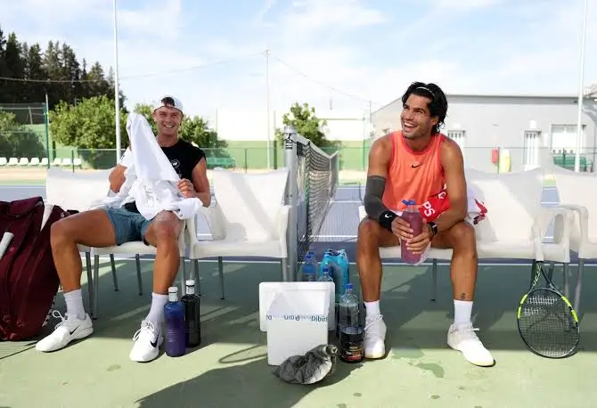 Two Tennis Players Relax And Smile Courtside During A Practice Session
