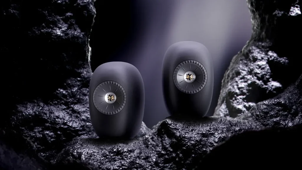 Matte black KEF LSX II LT speakers display on rugged black rocks in a dramatic studio setting, highlighting their sculptural design and metallic Uni-Q driver