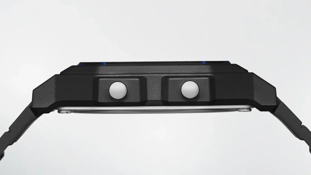 Side profile of the black Casio F-B100W case. Two round silver push-buttons sit on the right side of the angular resin case; the thin stainless-steel back and black resin strap lug are visible