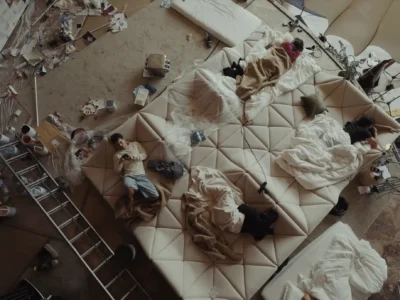 Overhead view of a sprawl cream geometric sofa covered with blankets, electronics, and people relaxing inside a clutter creative studio