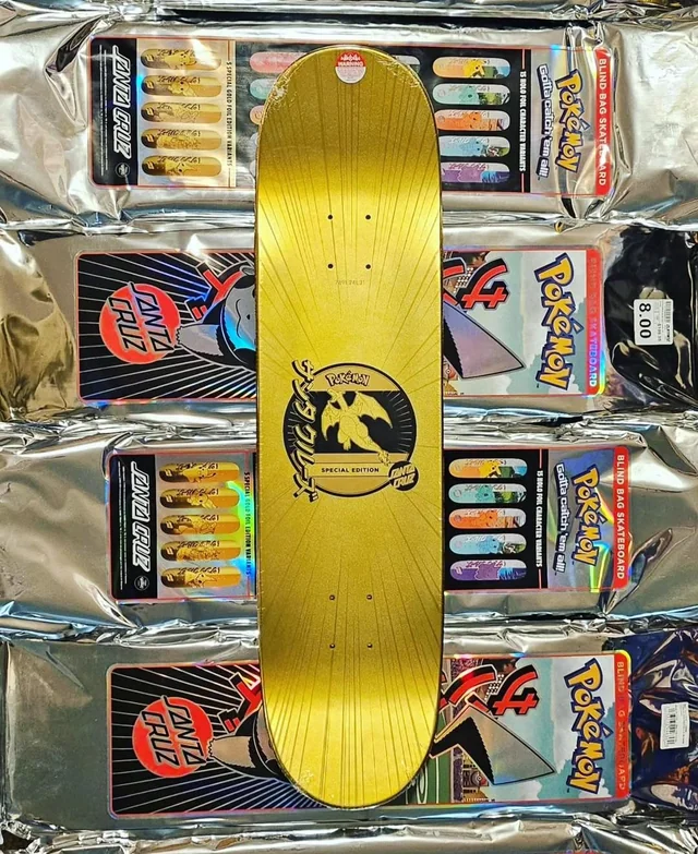 Gold Charizard Pokémon skateboard deck displayed over sealed Santa Cruz blind bag packages