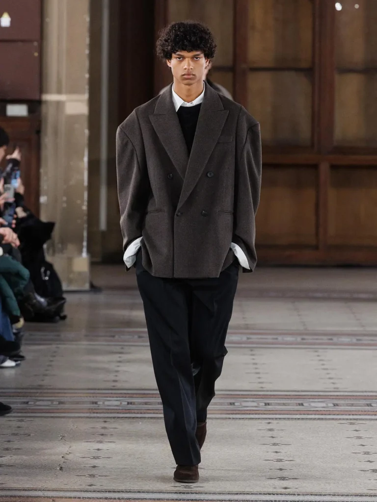 Model wearing a cropped brown double-breasted blazer over a white shirt and black knit, paired with tailored black trousers and brown suede shoe