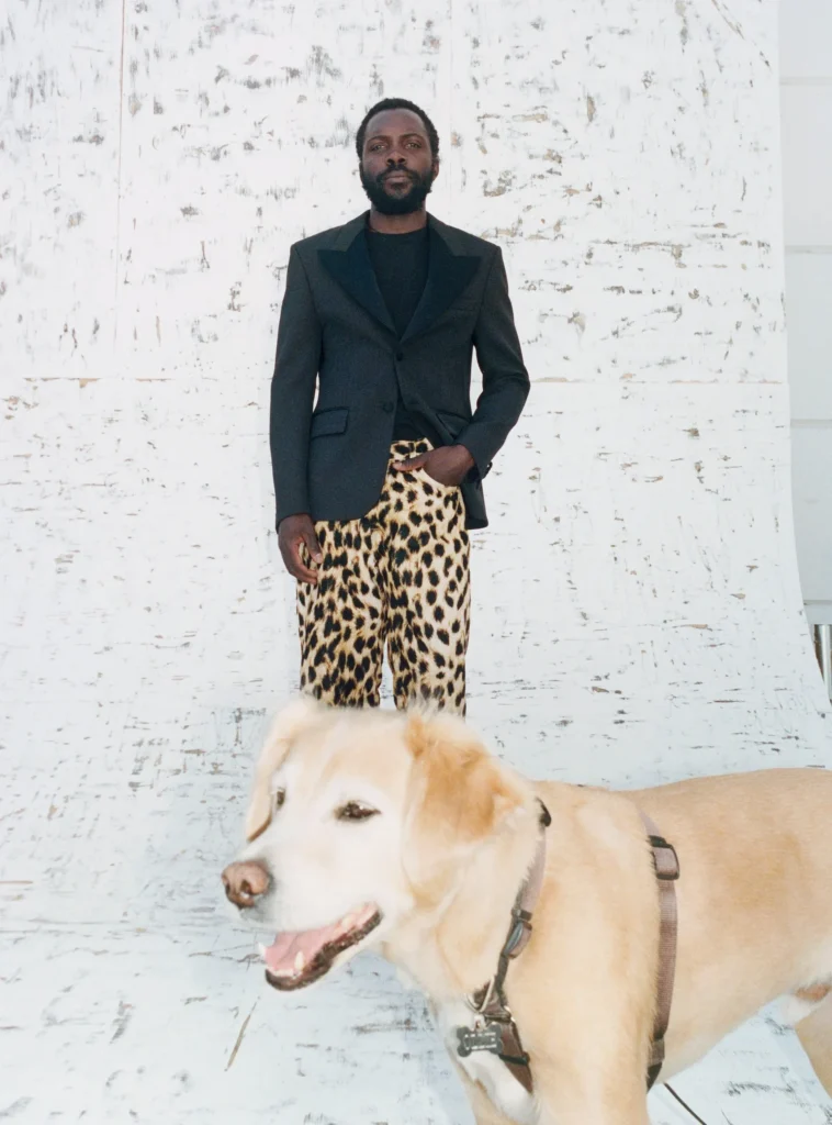 Person wear a black tailor blazer with leopard-print pants as a tan dog stand in the foreground