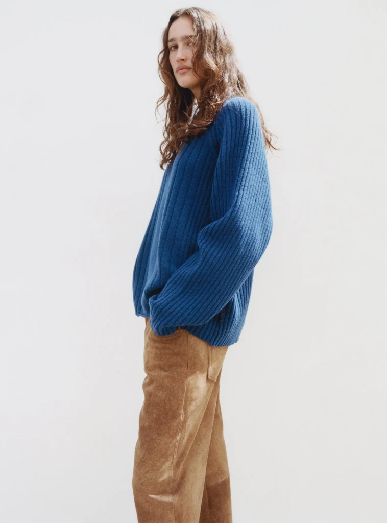 Person wear an oversize blue rib sweater with brown suede pant against a white background