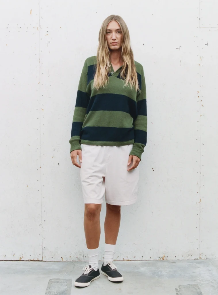 Person wear a green and navy stripe collared sweater with white short, white socks, and black shoe