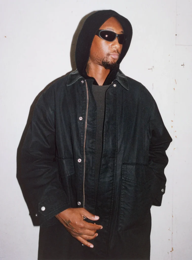 Person wear black sunglass, a black hooded jacket, dark knit top, and black pant