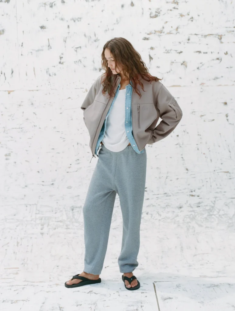 Person wear a crop gray jacket over a denim shirt and white top with gray sweatpant and black sandal