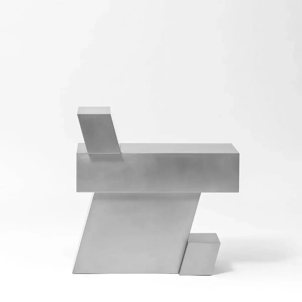 Side profile of a stainless steel sculptural chair by Hyunsin Ghwang, showing its flat triangular support panel and offset geometric blocks against a white background