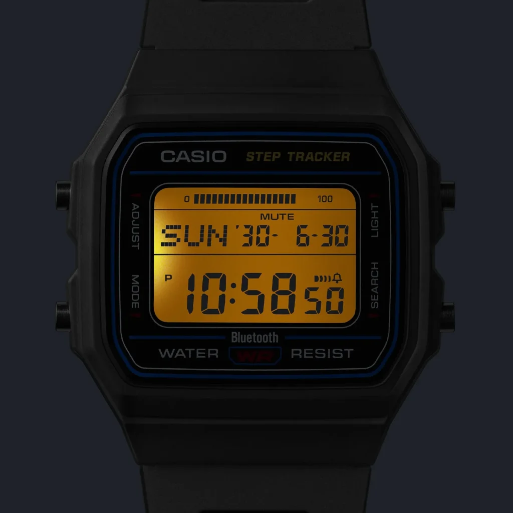 Close-up of the Casio Step Tracker face with the LED backlight on. The LCD glows amber-yellow and display Sunday 30, 6-30, time 10:58:50, a step-progress bar, MUTE indicator, and Bluetooth / WATER WR RESIST text on a black bezel with blue accent line