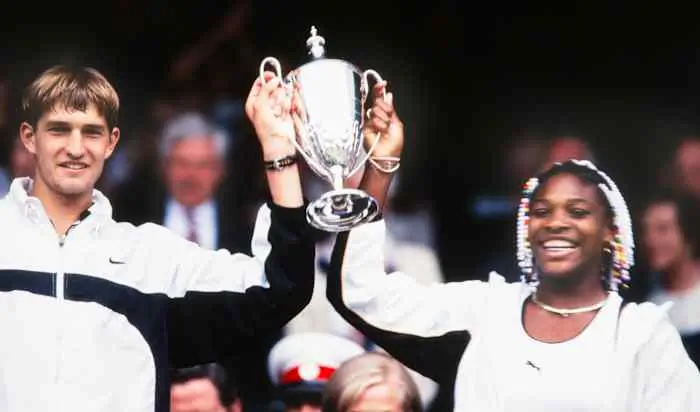 Two Tennis Players Celebrate Together While Holding A Championship Trophy