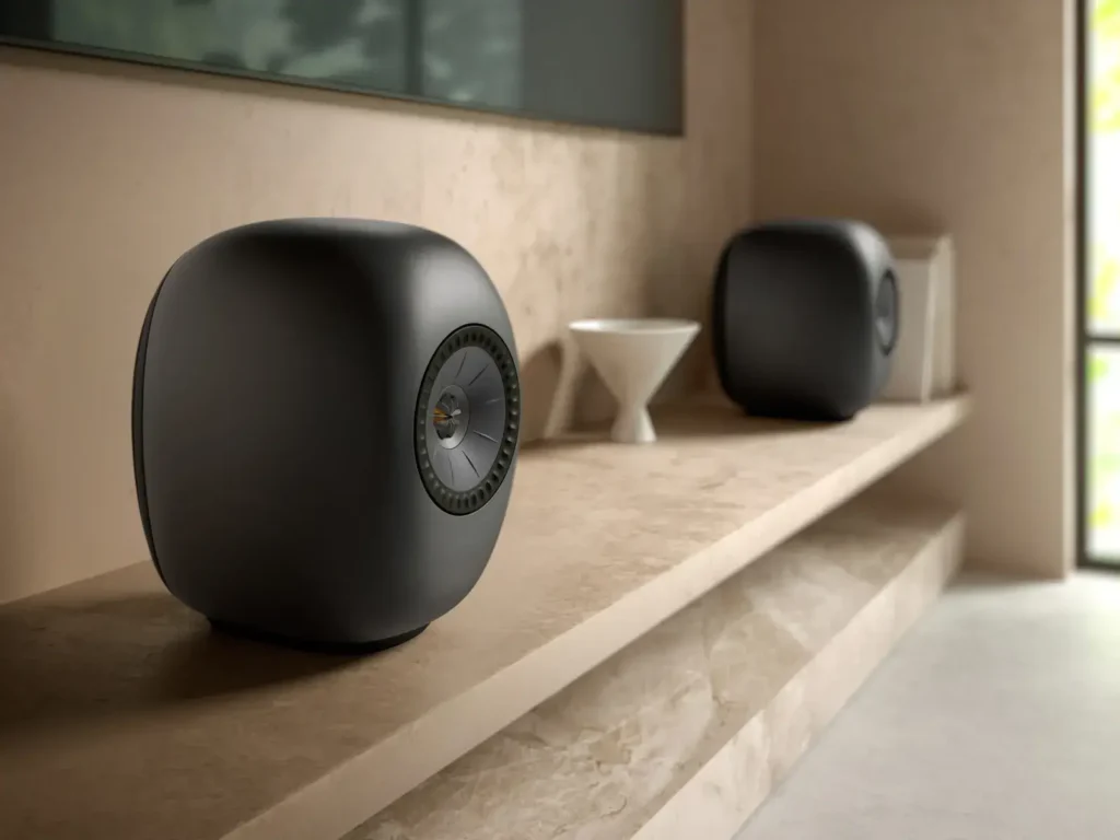 Close-up of matte black KEF LSX II LT speakers resting on a stone shelf in a modern interior, emphasizing their compact design and premium finish