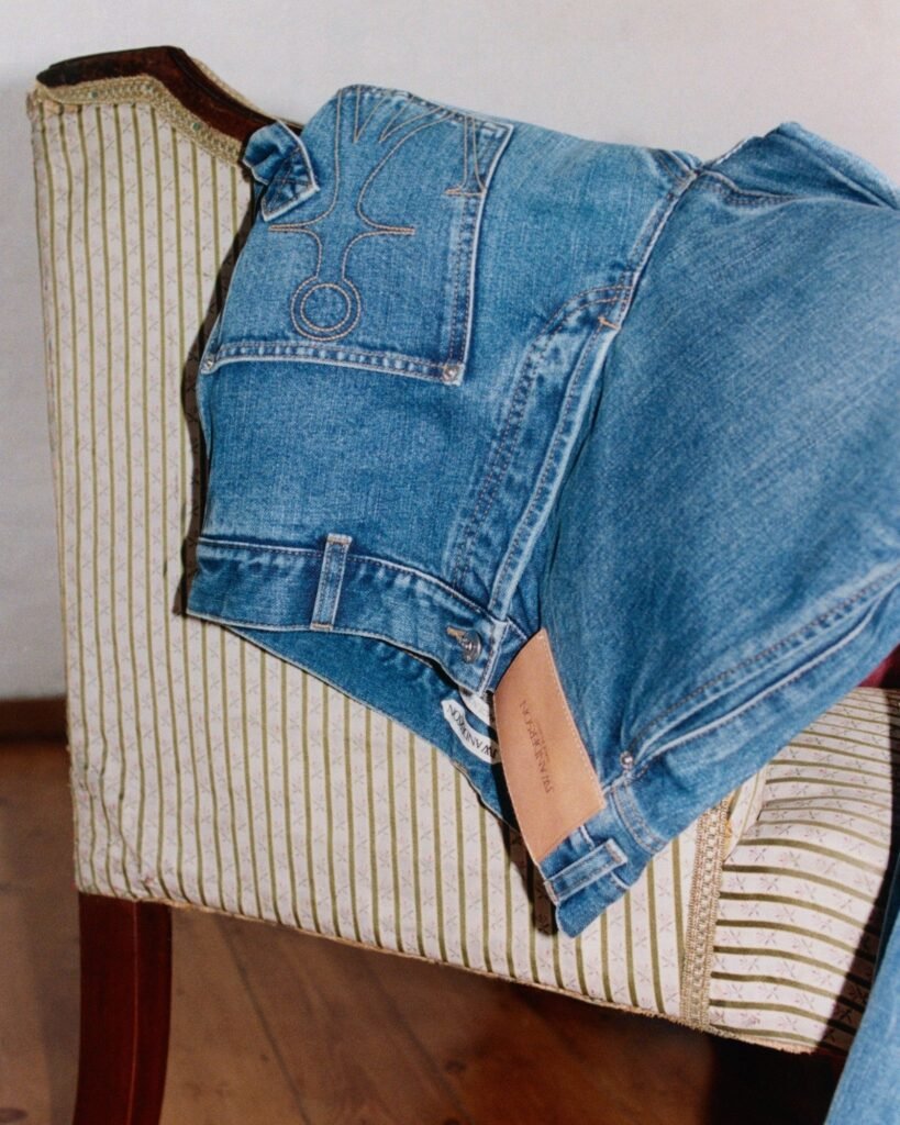 Blue denim jacket draped over a green-and-white striped upholstered chair, with a geometric stitch pocket and leather tag