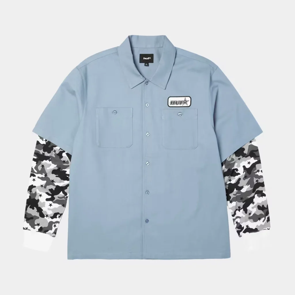 Light blue HUF short-sleeve button-up shirt with two chest pockets and gray camouflage-patterned long sleeves beneath it