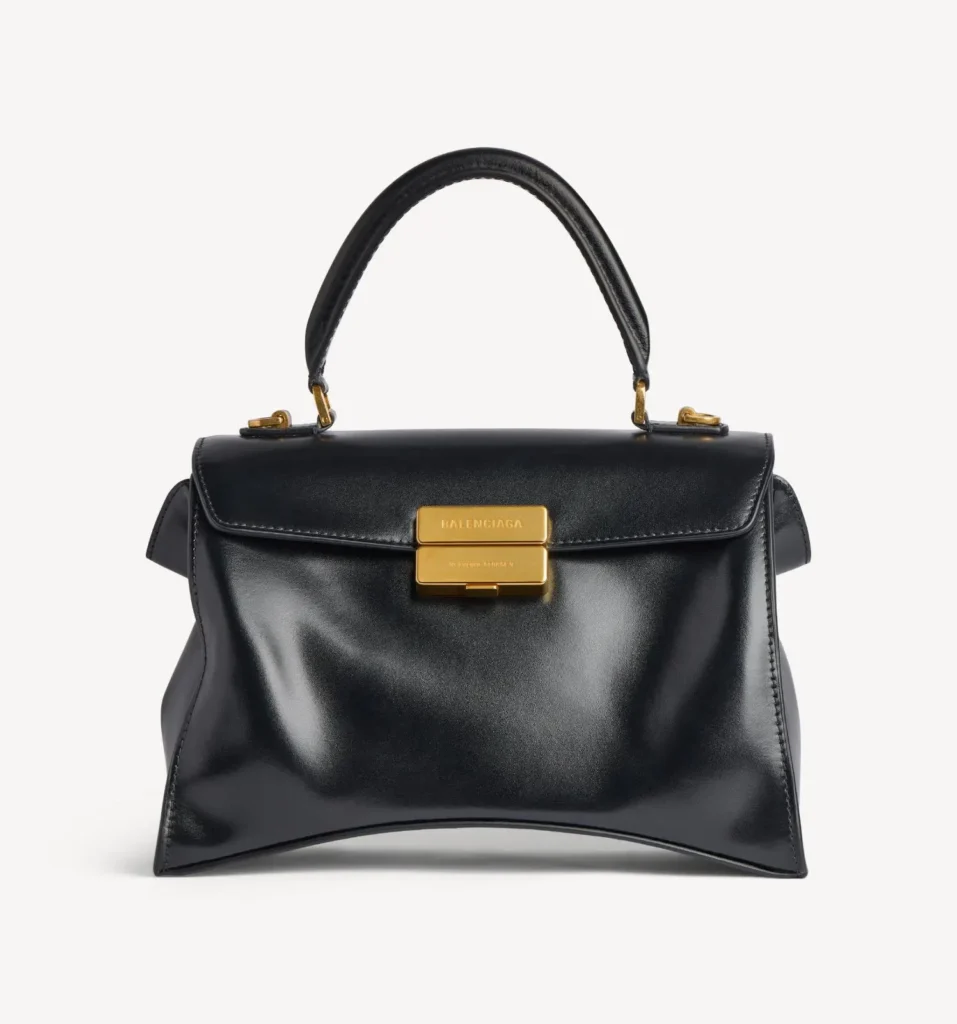 Black leather Balenciaga handbag with a curved top handle and gold clasp, centered against a white background