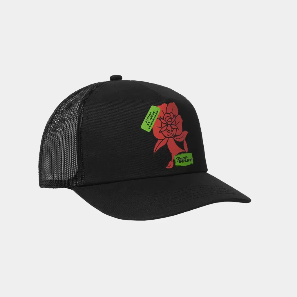 Black mesh-back trucker cap with red cartoon flower graphic and green label patches on a light gray background