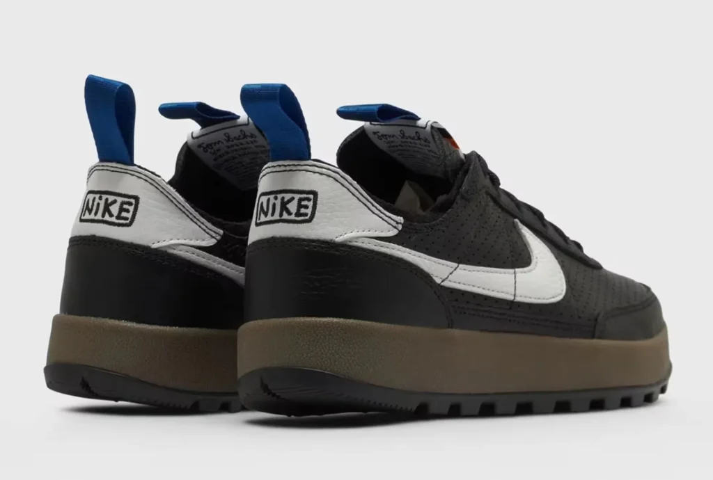 Pair of black Nike shoe with white swooshes, brown midsoles, black lugged soles, and blue pull tabs on a white background