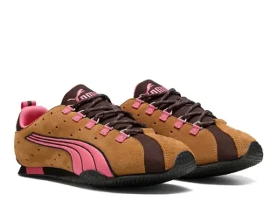 Pair of brown and black Puma shoe with pink Formstrip accents, pink lace loops, and rugged black soles on a white