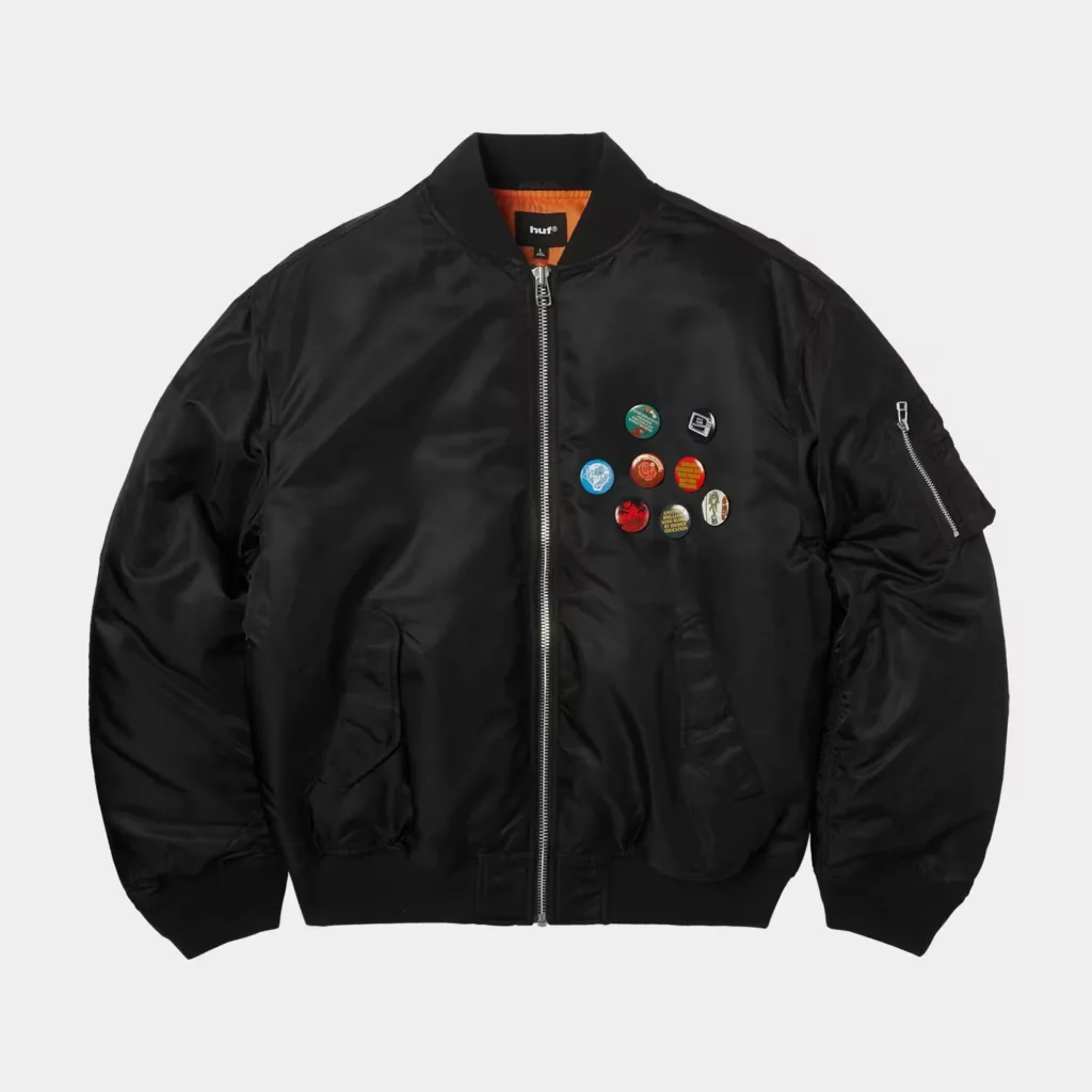 Black satin bomber jacket with orange lining, front zipper, utility sleeve pocket, and colorful circular pins on the chest