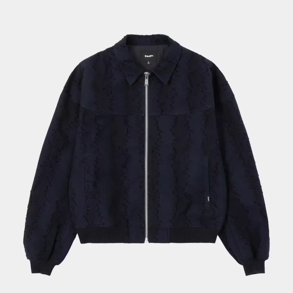 Black HUF jacket with an allover textured pattern, pointed collar, silver front zipper, pockets and ribbed cuffs and hem