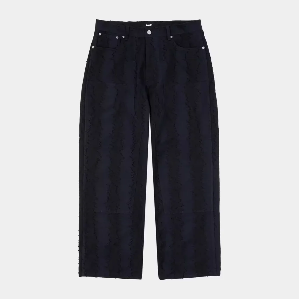 Black HUF trousers with silver rivets, front pockets, and a subtle tonal all-over pattern on a light gray background