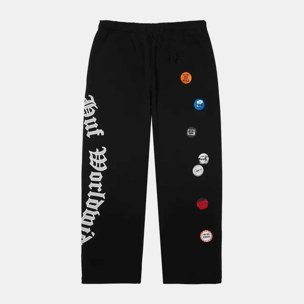 Black sweatpants with white gothic lettering down one leg and colorful circular patches on the other, shown against a light