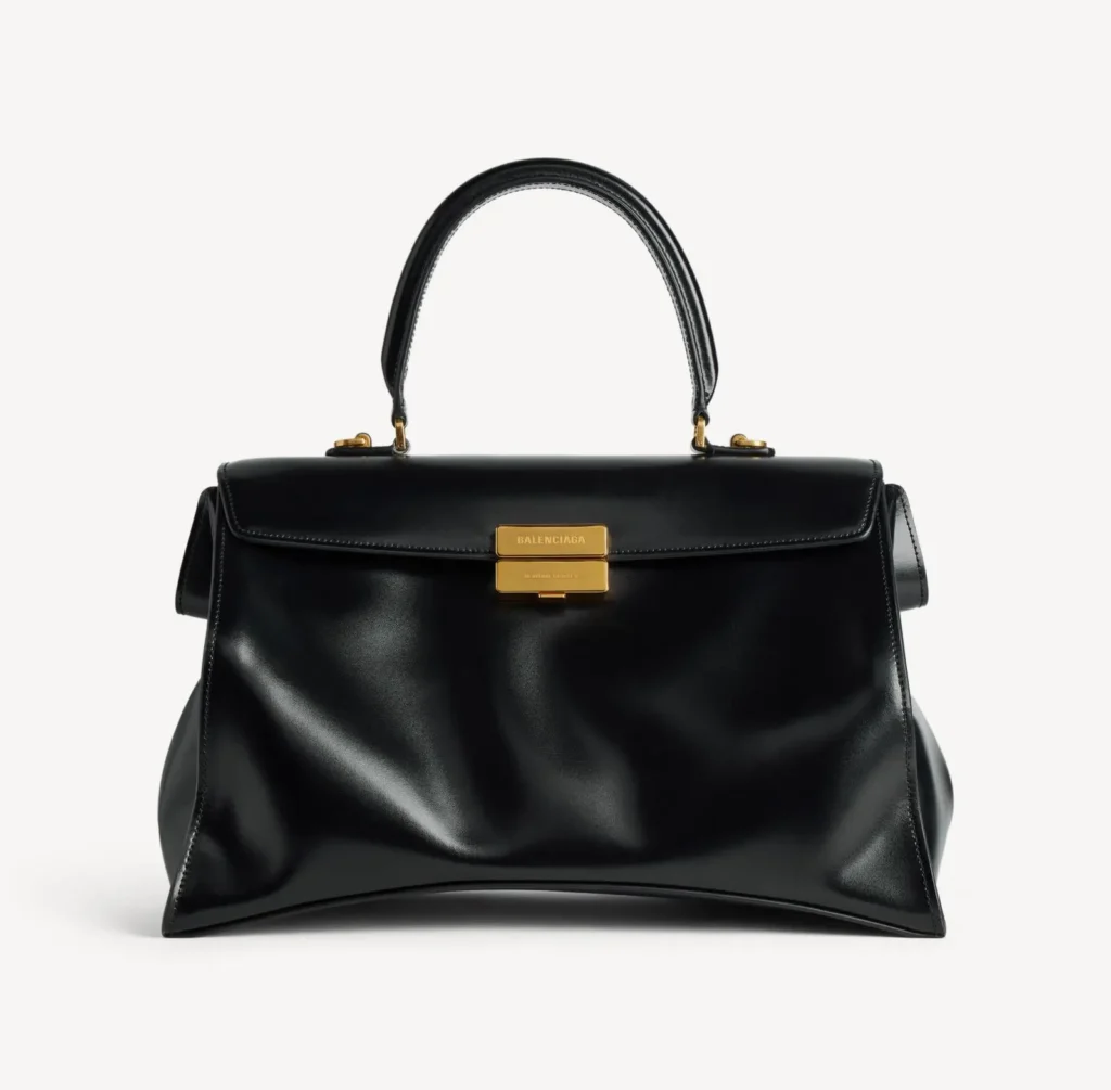 Black leather Balenciaga handbag with a top handle and gold clasp, centered against a white background