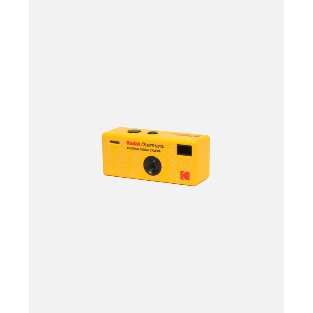 Yellow Kodak Charmera keychain digital camera with black lens and screen on a light gray background