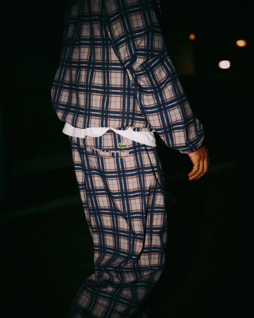 Cropped figure walking in a navy-and-white plaid jacket and trousers, with a white shirt hem and green crocodile logo at the