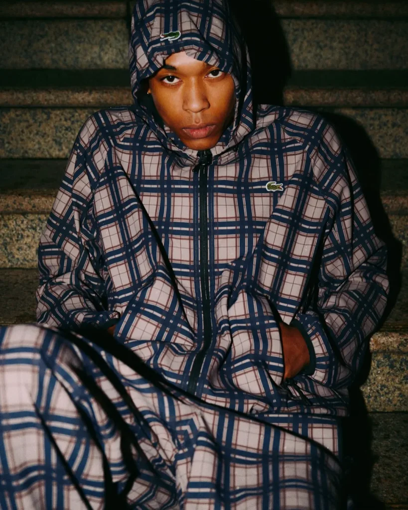 Person seated on steps in a blue-and-beige plaid hooded jacket and matching pants, staring at the camera