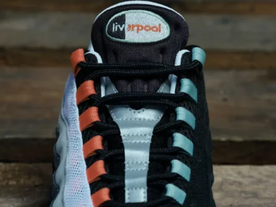 Close-up of a black and white sneaker with orange and teal lace loops and a Liverpool tongue logo on wooden planks